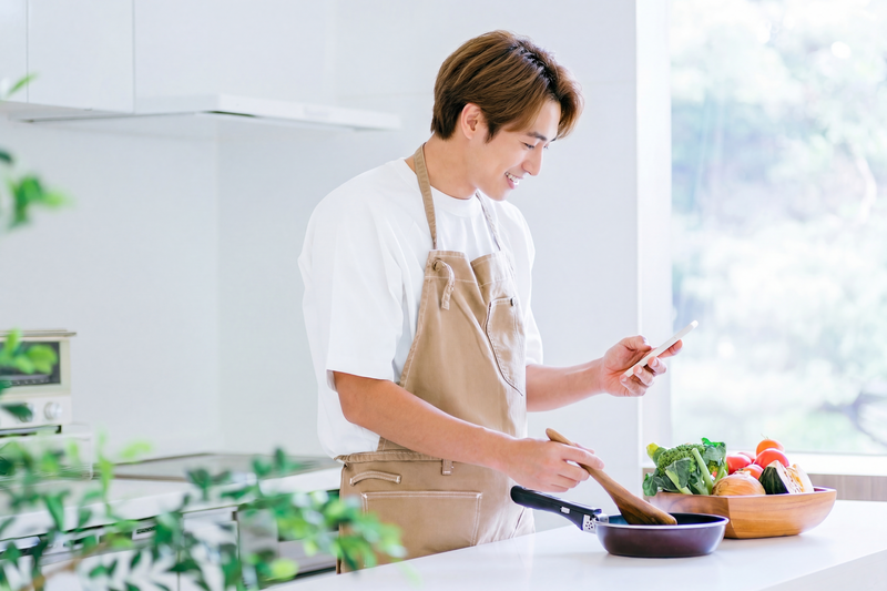 スマホでレシピを見ながら料理する男性のイラスト