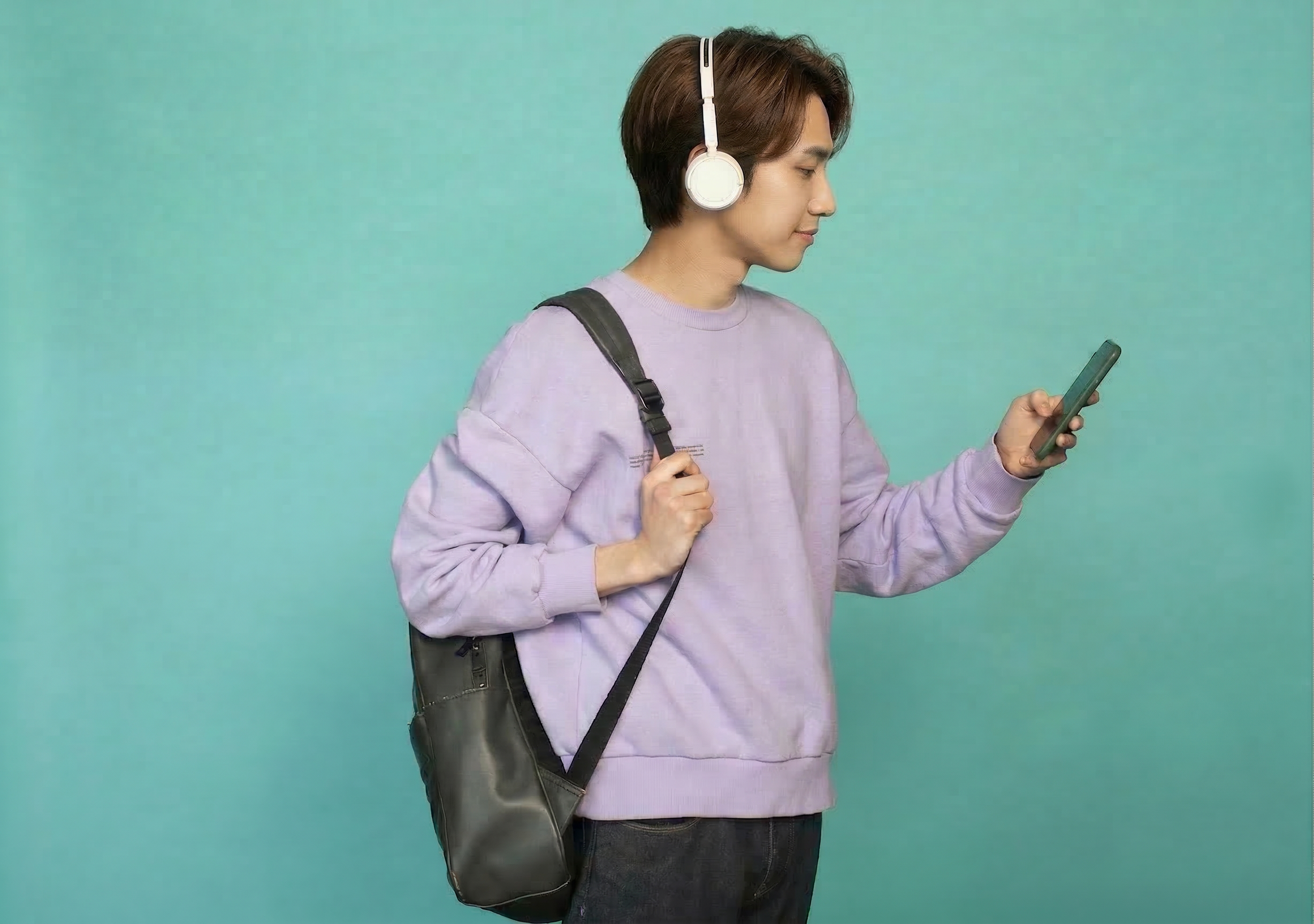 ヘッドフォンとバッグを持ちスマホを見る男性