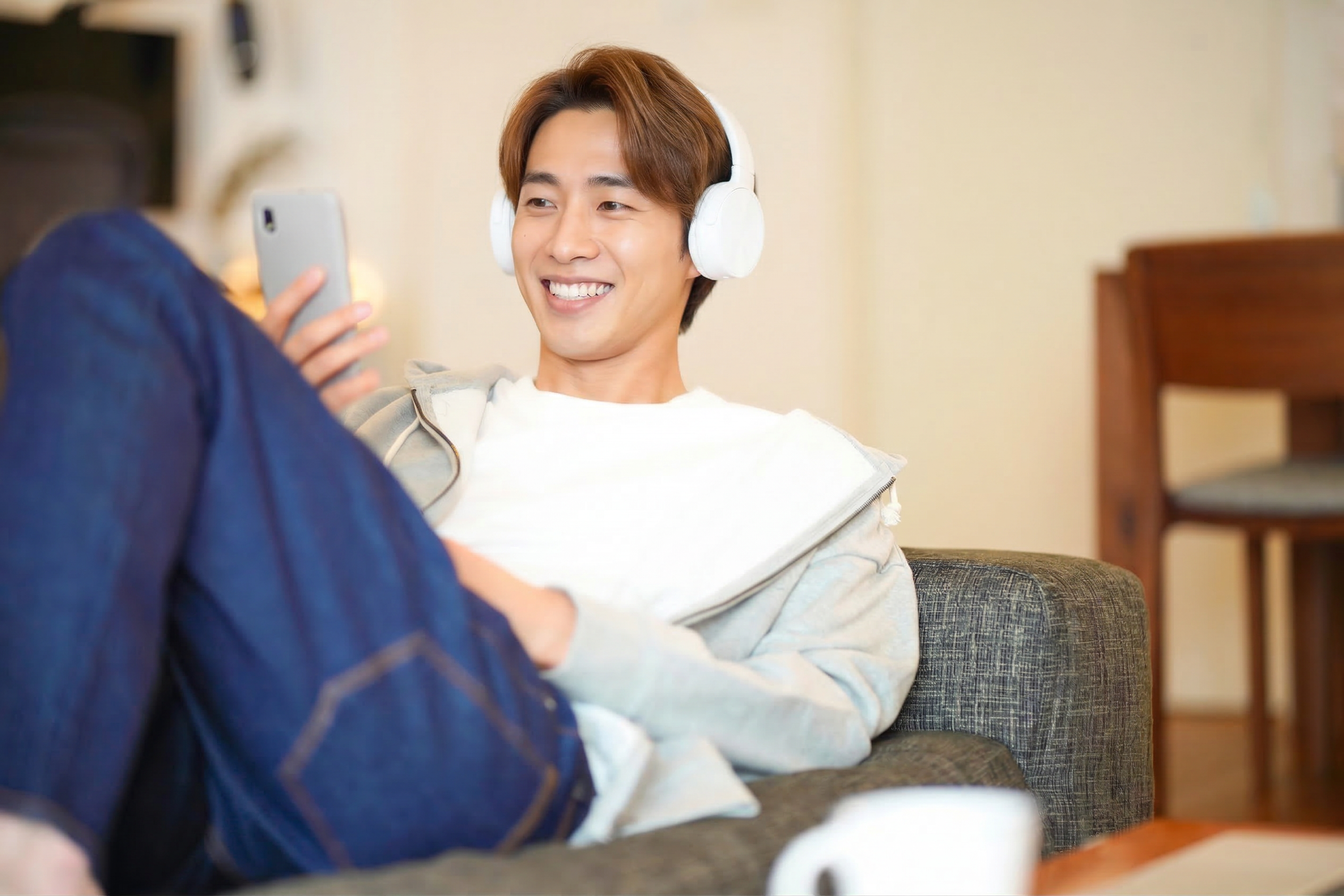ソファでヘッドフォンをしてスマホを見る男性