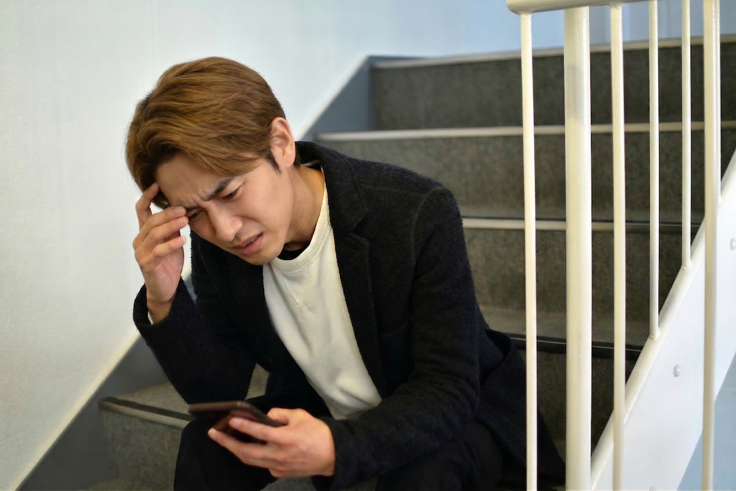 階段でスマホを見てストレスを感じる男性